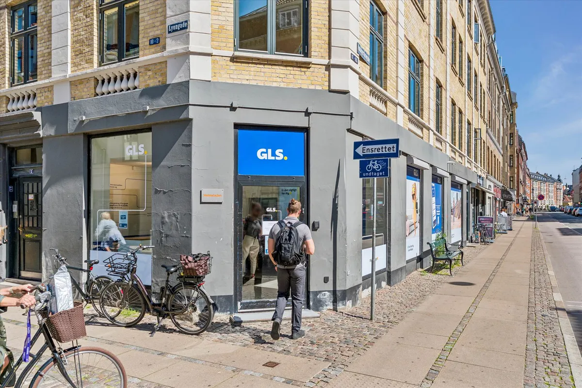En mand går ind i en GLS butik, der ligger på en gågade med flere cykler parkeret udenfor