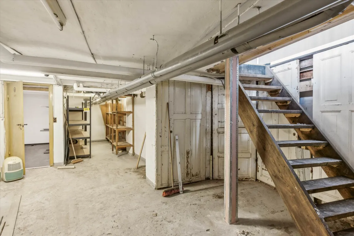 En gammel nedrejte med trætrapper og hvide vægge, gamle døre og et skur, gulve og loft med røre og støv