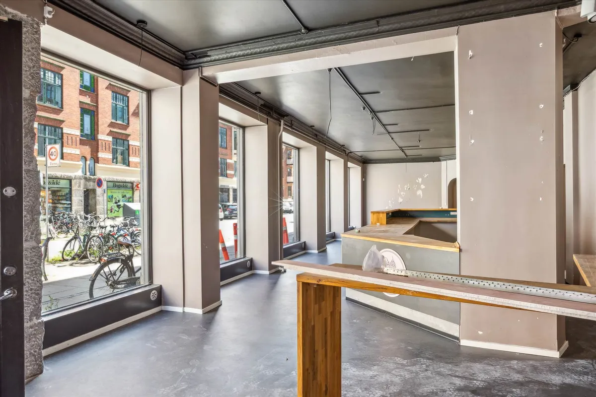 Store vinduer og glasdøre i en nyindrettet lokale med åbne gulv og loft samt en arbejdsbank og en væg med uregelmæssige
