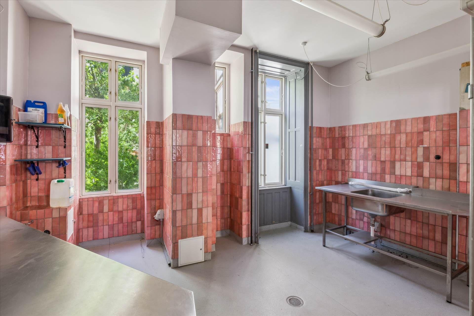 En stor vaskeri med røde kakelede vægge og lyseruder og et tøjvaskestativ og en vandflaske og en sprayflaske på hylden