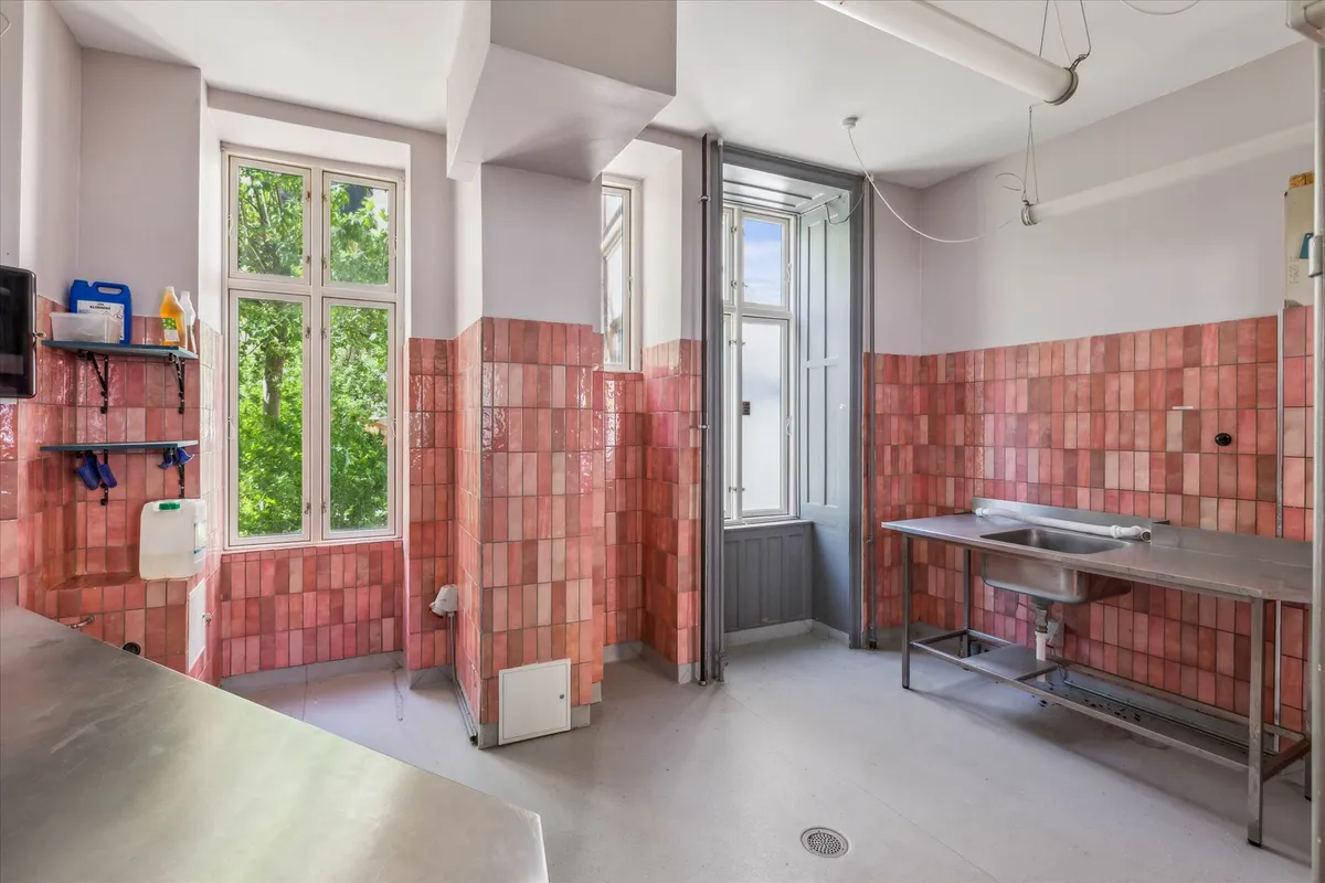 En stor vaskeri med røde kakelede vægge og lyseruder og et tøjvaskestativ og en vandflaske og en sprayflaske på hylden