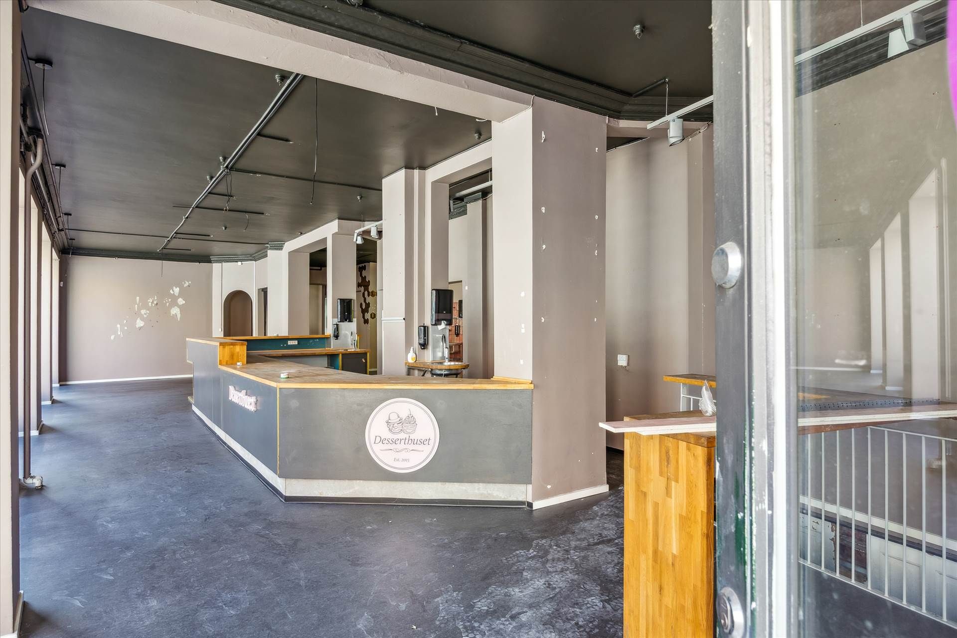 Indenfor et tomt lokale med en høj loftshøjde og et åbent gulv. En simpel receptionsbord med et logo og et stel med