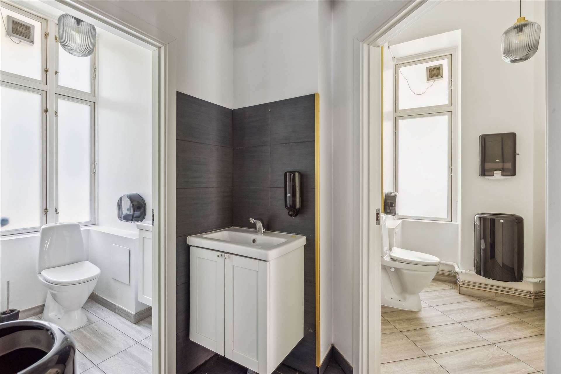 To toiletrum med hvide toiletter og hvide vasketøjsskabe med en hvid vask og lysegrå vægge og loft