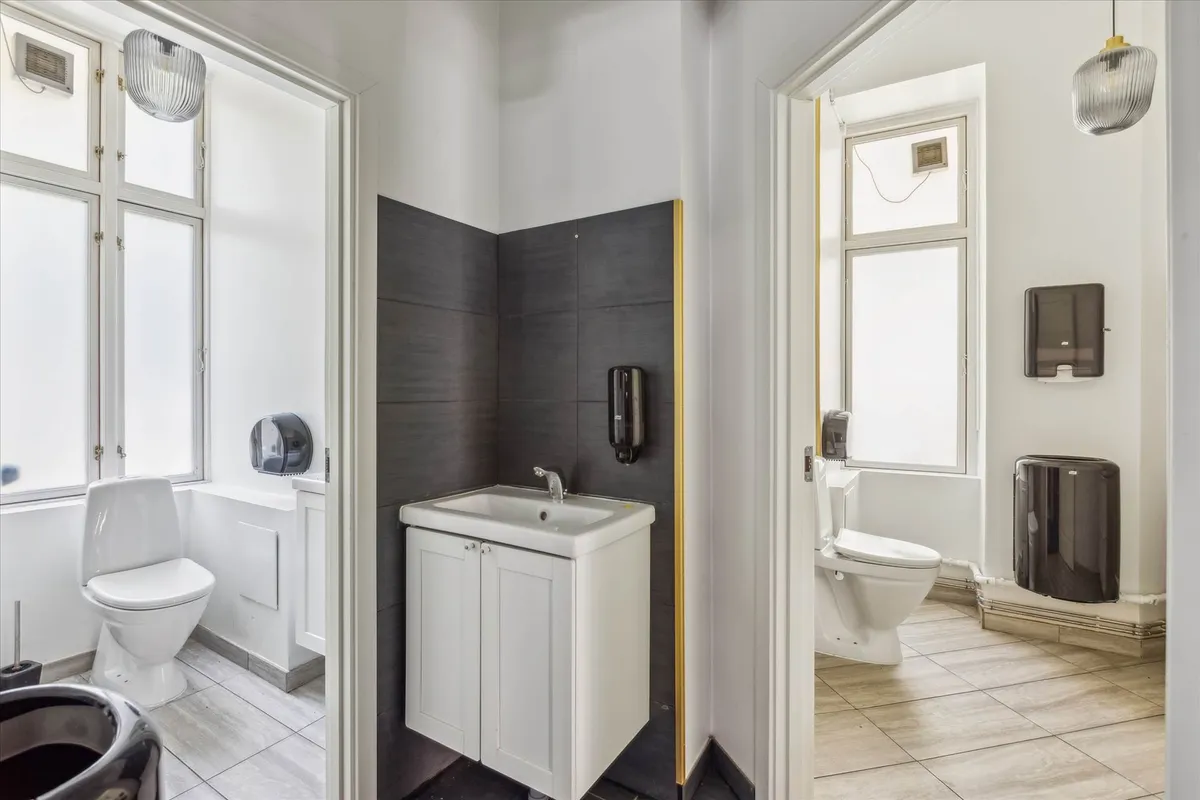 To toiletrum med hvide toiletter og hvide vasketøjsskabe med en hvid vask og lysegrå vægge og loft