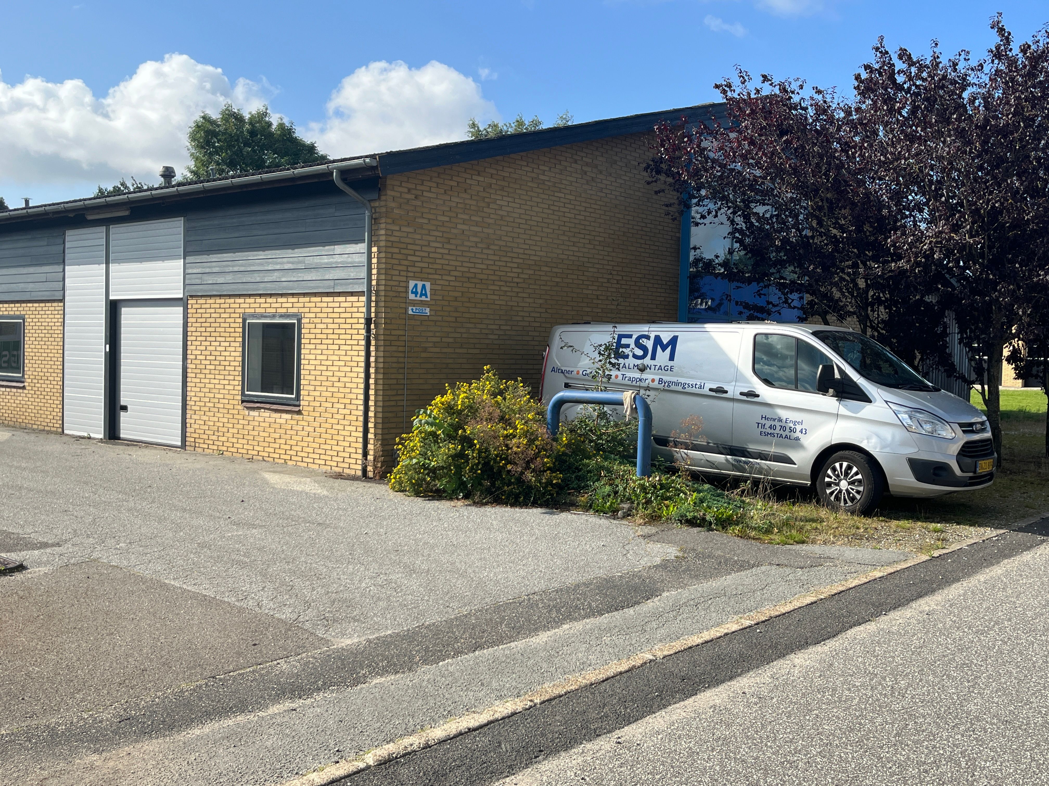 En hvid servicevogn fra ESM Altinget parkeret ved siden af et erhvervslejemål, der ligger i et større erhvervspark i