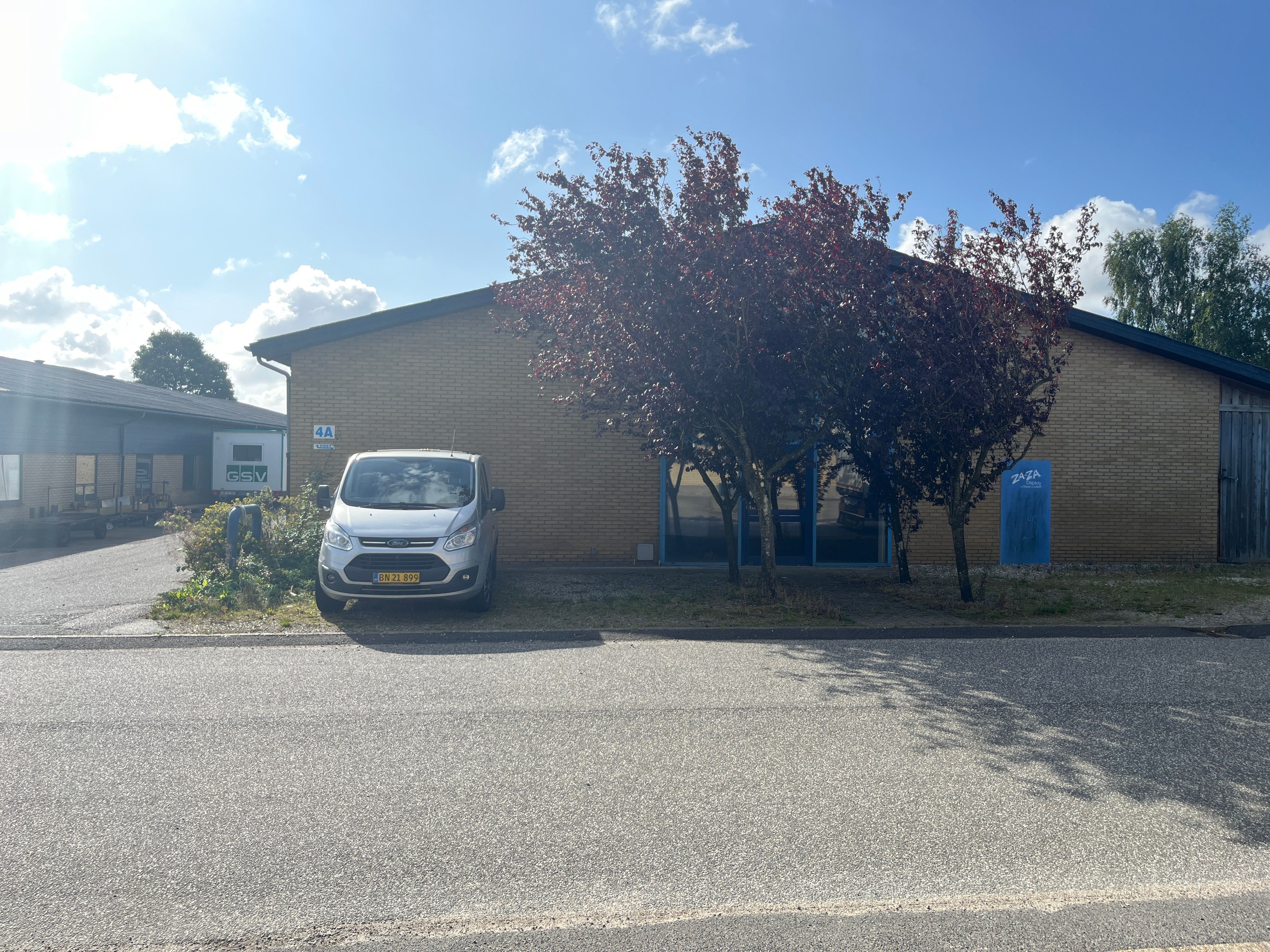 Et forretningslokale med røde mursten og en forhøjede indgang med nummer 4A. Der er en forhøjede campingvogn parkeret foran.