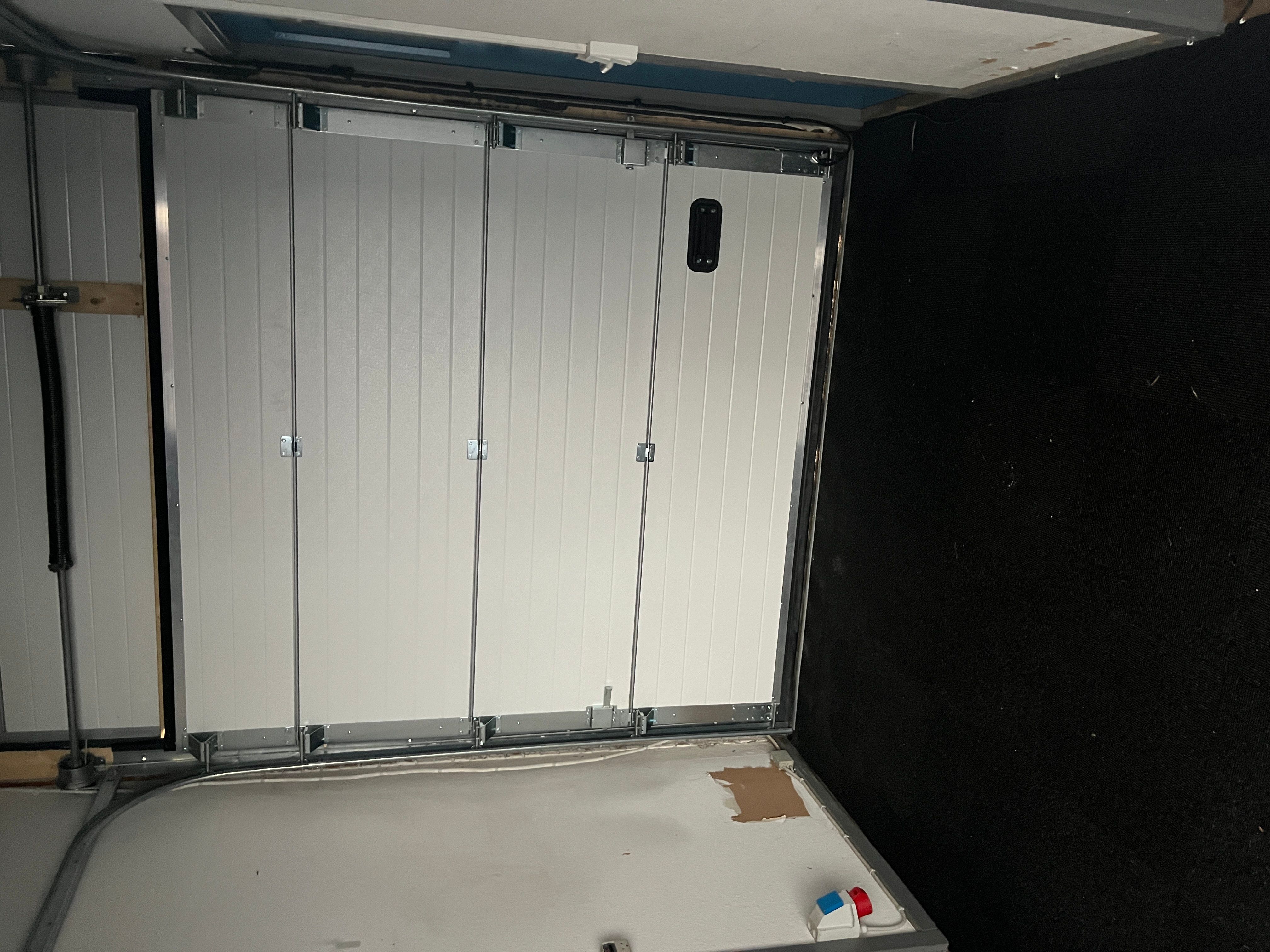 Garage med hvide vægge og gulv samt to store hvide sektioner med håndtag og drejemekanismer til døre