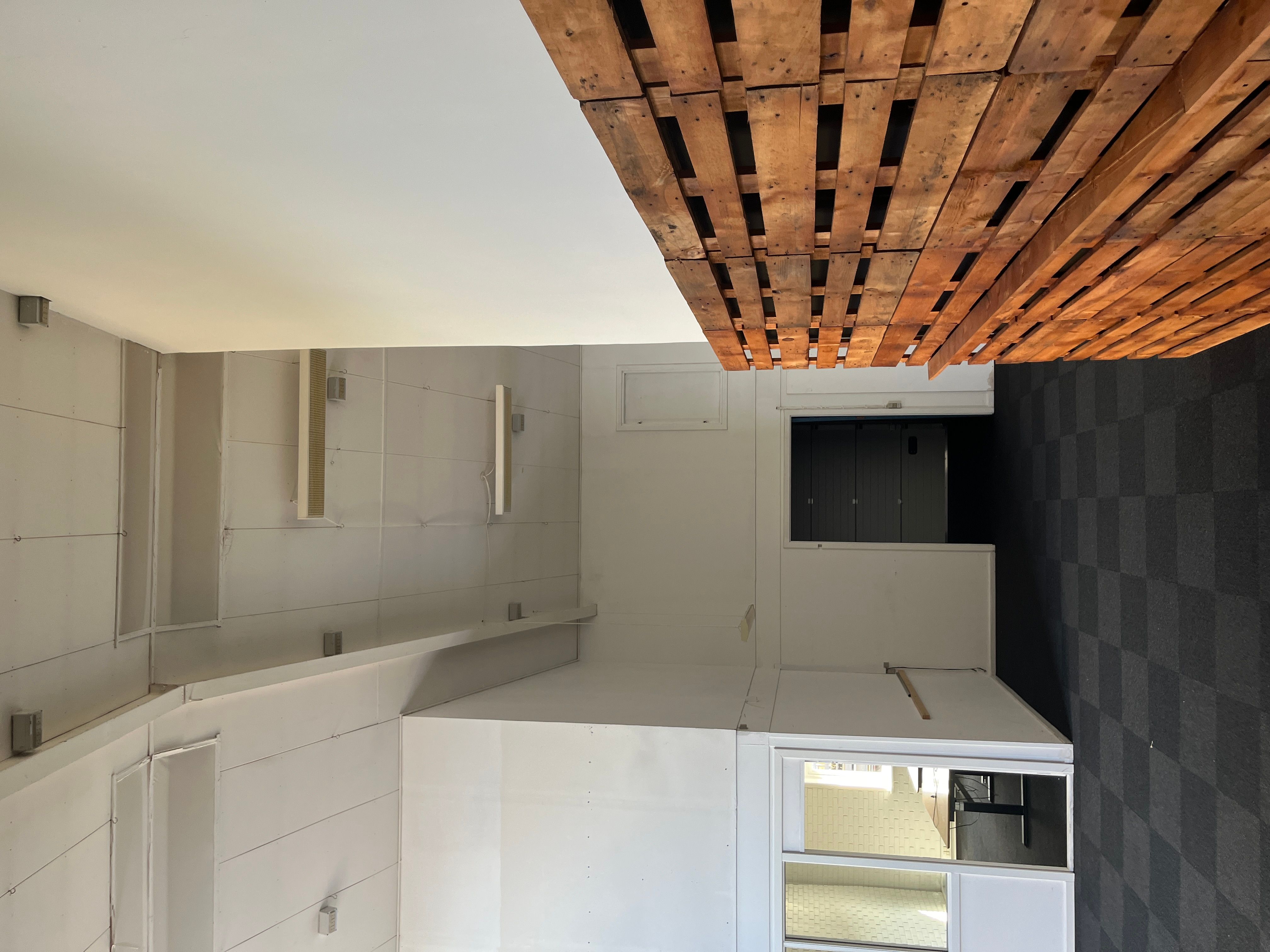 Rum med hvid og brun loftskonstruktion, mørk gulvbelægning og hvide vægge med vinduesåbninger og døre