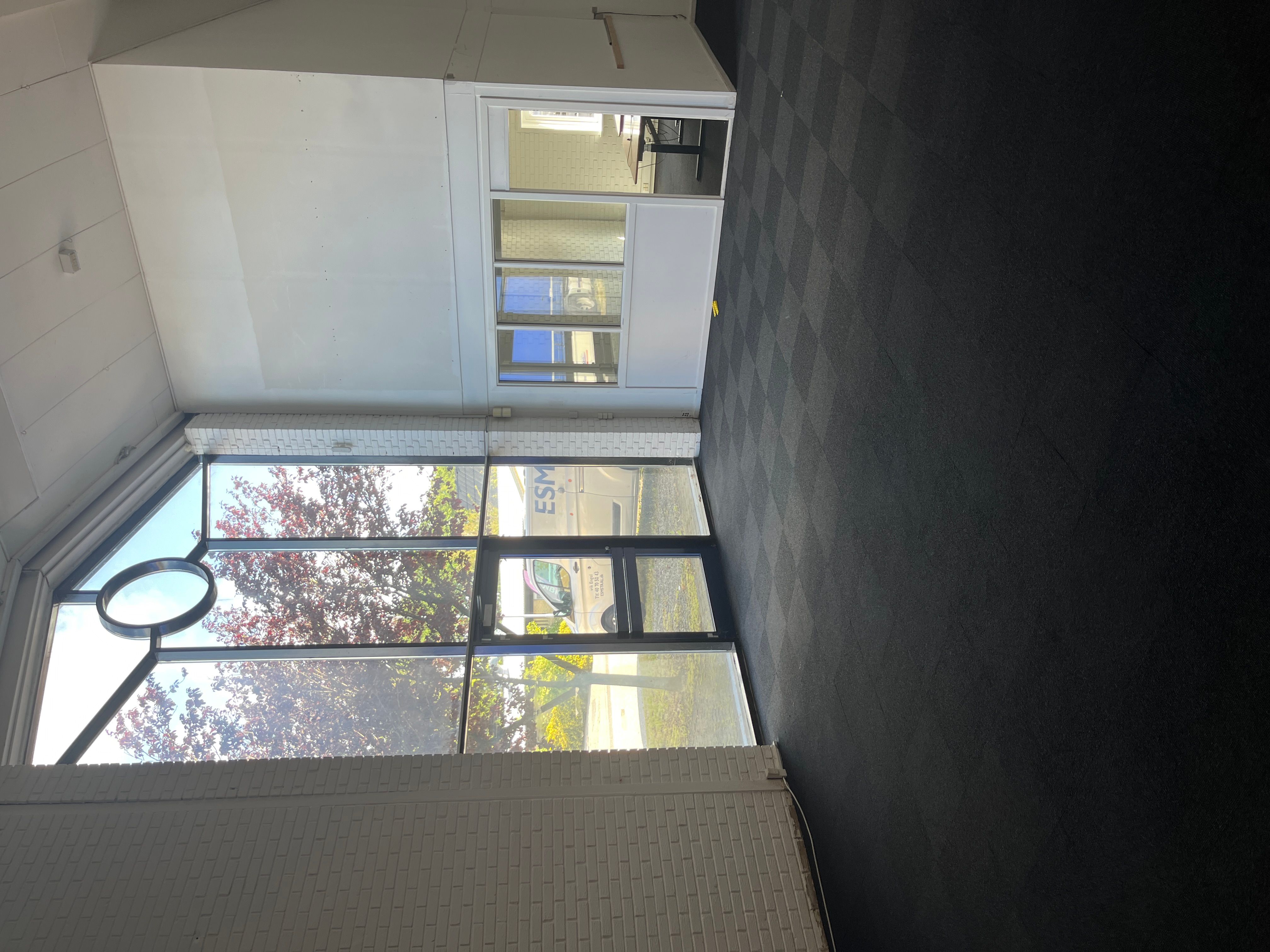 Et erhvervslejemål med store ruder og højloft er indrettet med mørke gulvbelægning og hvide vægge. Rummet er lyse og