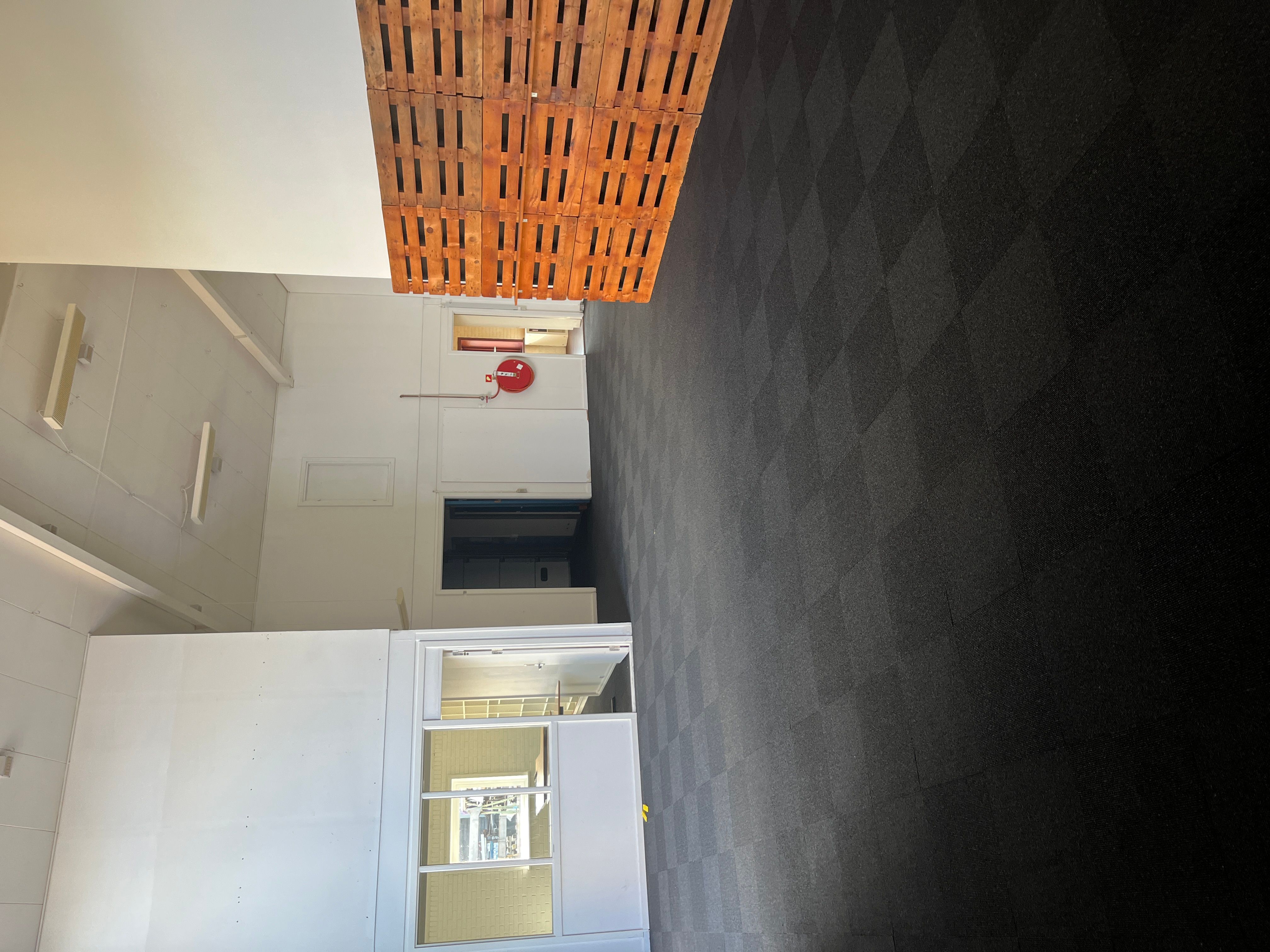 Væg med hvide paneler, gulv og loft. Træpalle og brandlæssere. Vindue og dør.