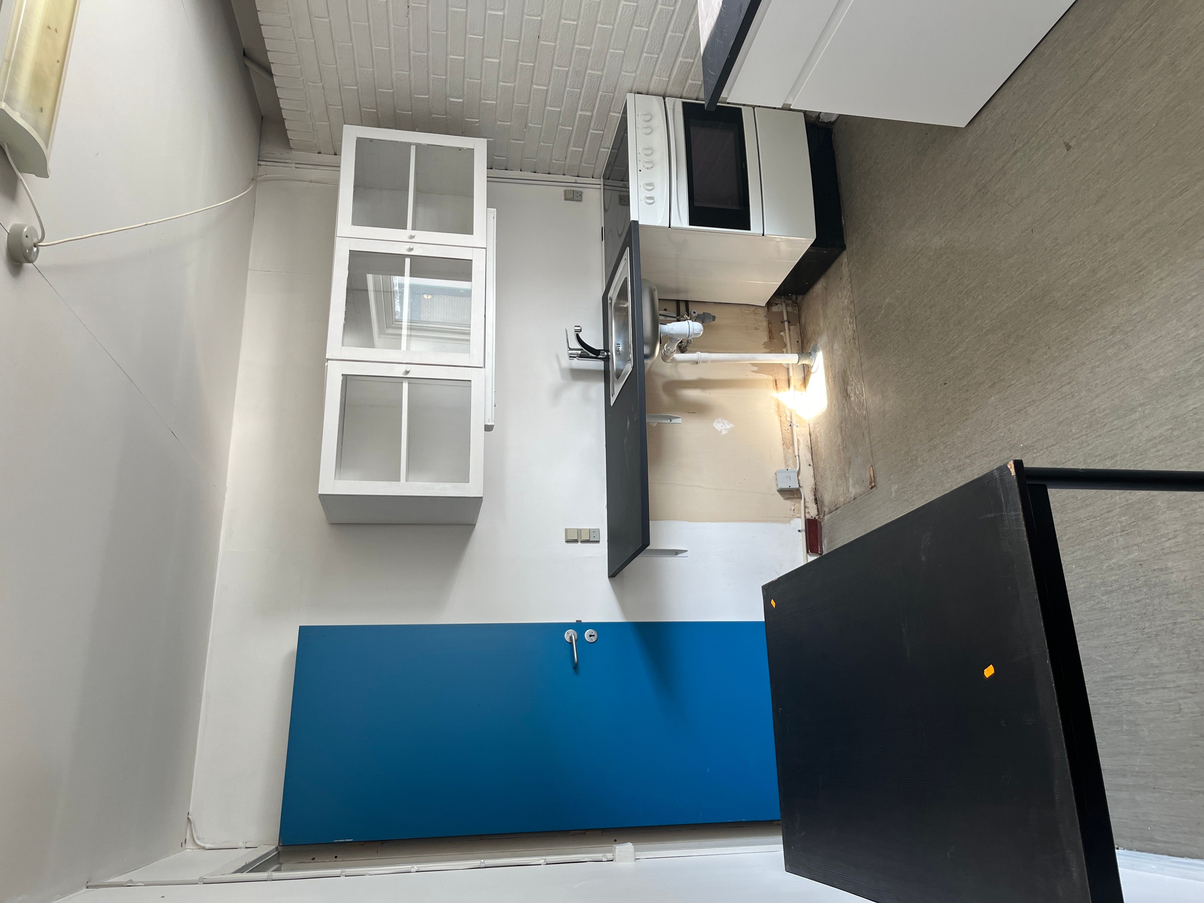 Køkken i et erhvervslejemål med højloft, to hvide vægskabe og et højt sort bord.