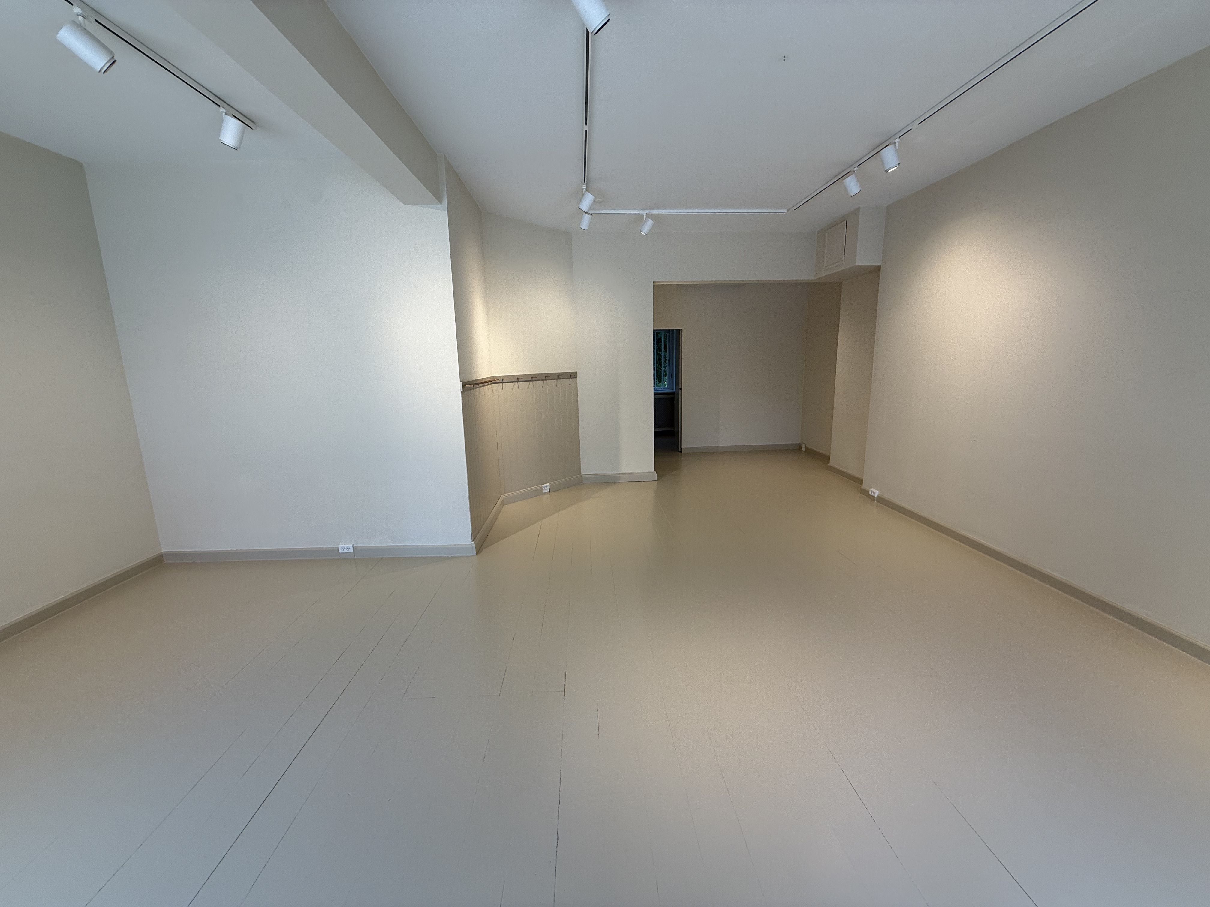 Butikslokaler med lyse gulve, vægge og loft samt åbning til en anden rumlig del af bygningen