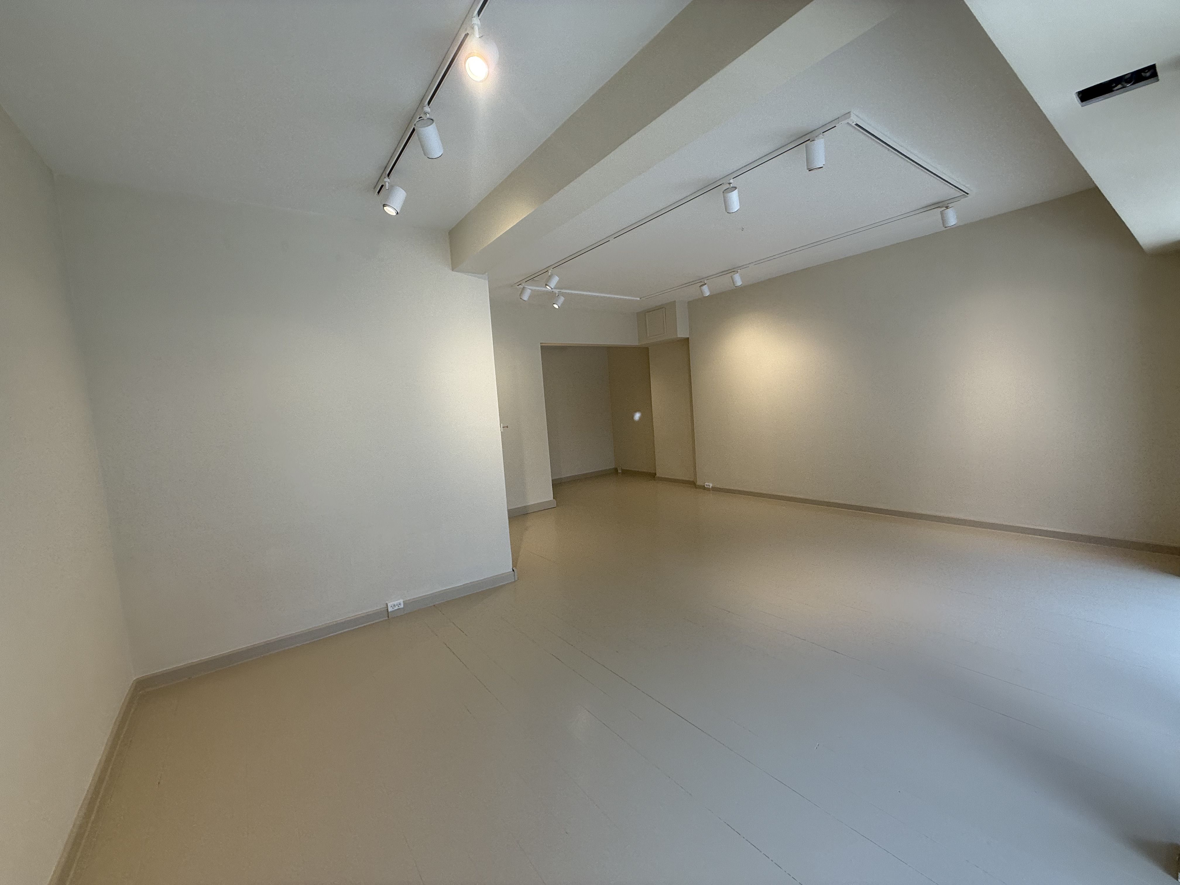 En tom og lys værkstedslokal med hvide vægge og gulv samt fire lysekroner i loftet
