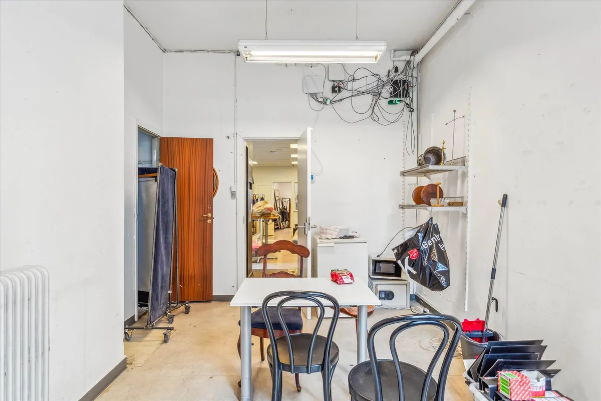 Genbrugsbutik med åbne døre, stolpebord, hængselsskabe og lysekroner samt salgsstativ og salgskasse