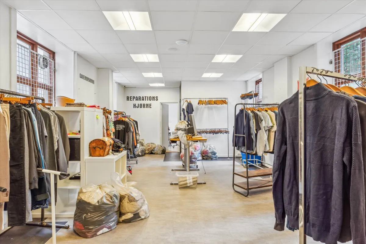 Forretning med tøj på hængere og på hylder, der er opdelt med håndskrevne skilte