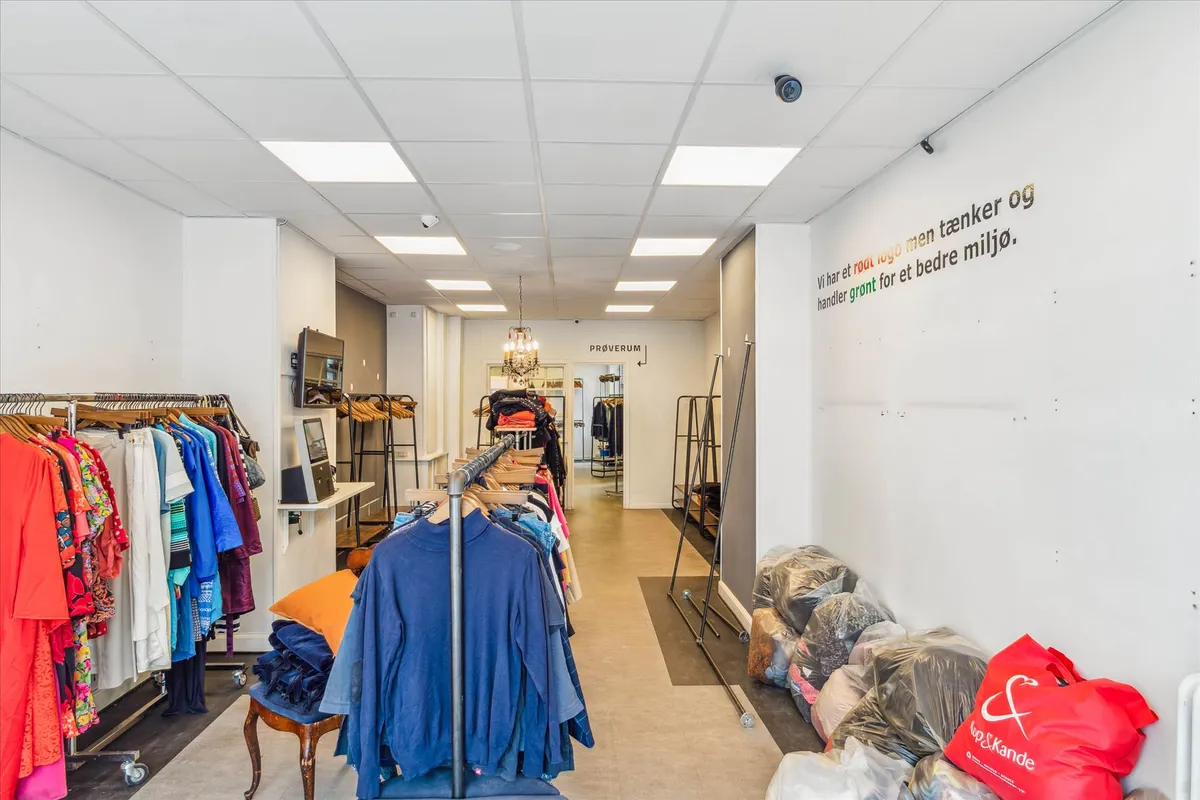 Butik med klæder og tøj på reoler og væggen med tekst og røde poser