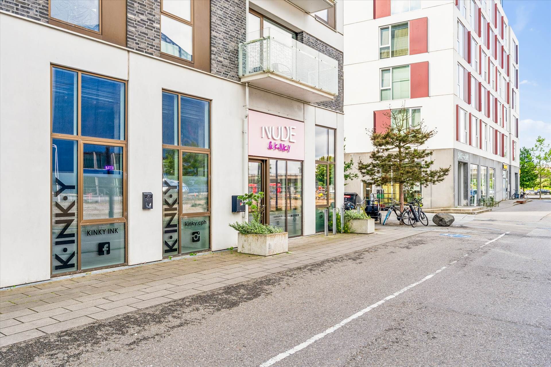 Lejemål på Amagerfælledvej 130 med store vinduer og pink skylting. Indvendig gård med grønne planter og parkerede cykler.