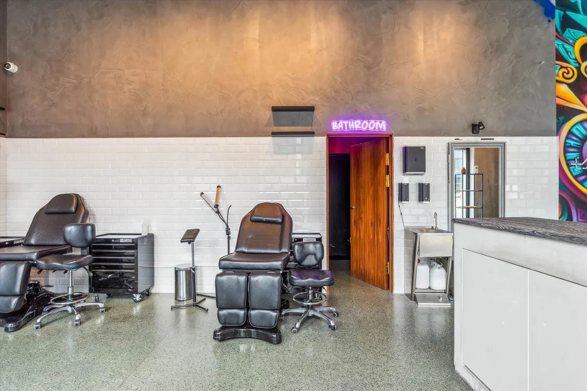 Inde i en stilfuld tatoveringssalon med højloftede lofter og moderne design, med to læderstole og to vasker.