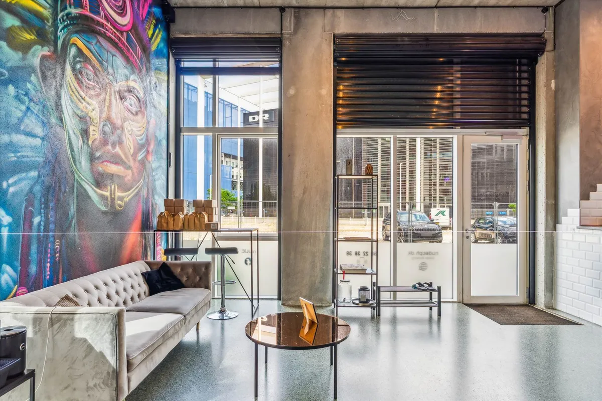 Butik med stort graffitimaleri, hvid sofa, gulvtæppe, rundt bord, gulvbelægning og glasdøre med refleksioner fra biler