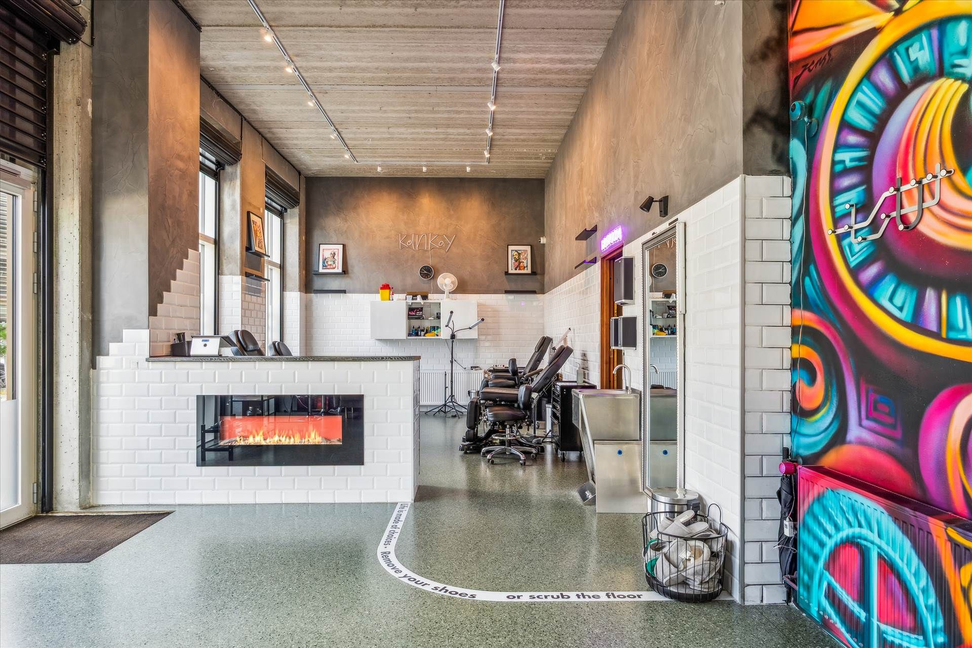 En skøn og moderne salon med en åben ildpejs, en stor malet væg, lyse pærer og en indgang til en separat del af salonen.