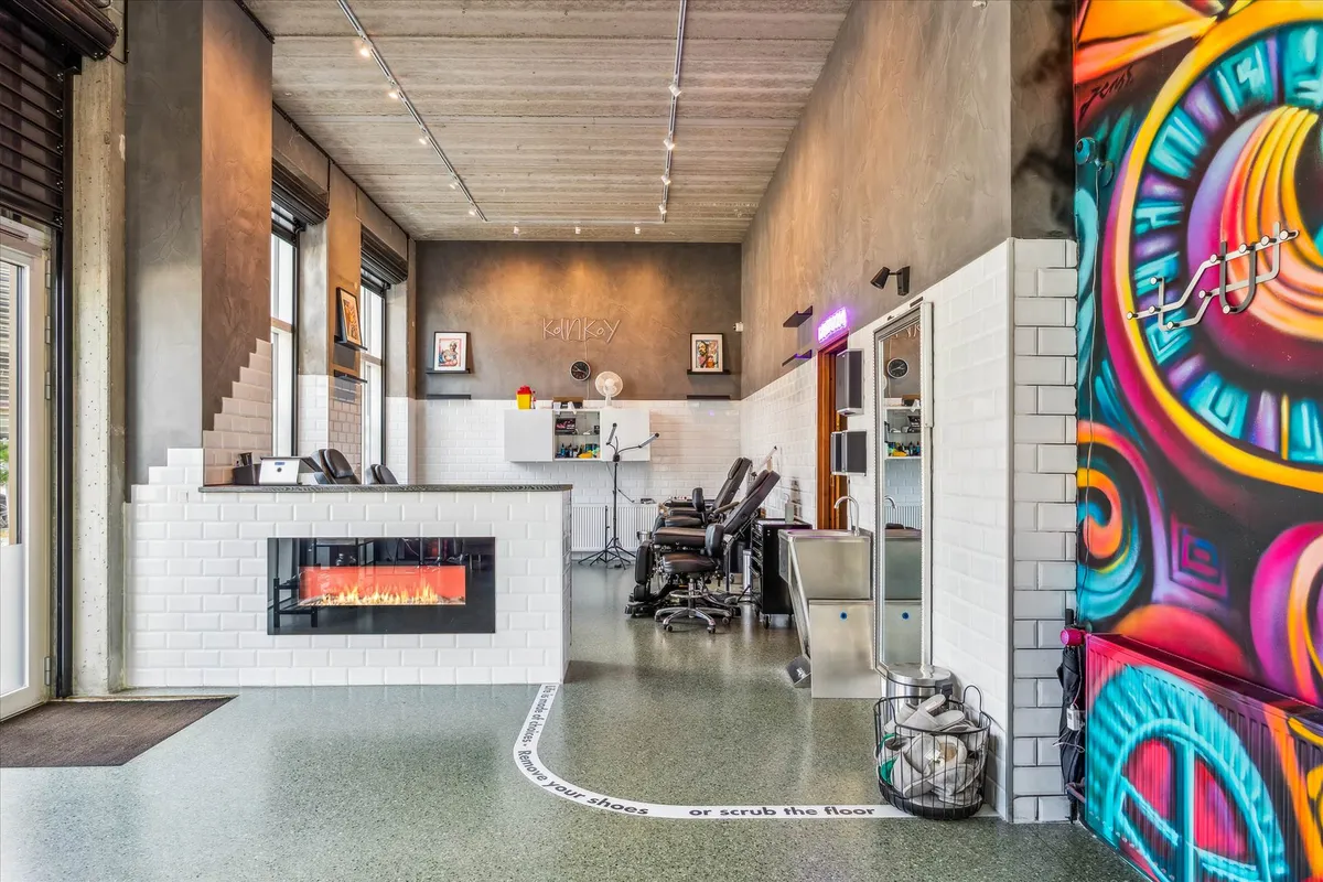 En skøn og moderne salon med en åben ildpejs, en stor malet væg, lyse pærer og en indgang til en separat del af salonen.