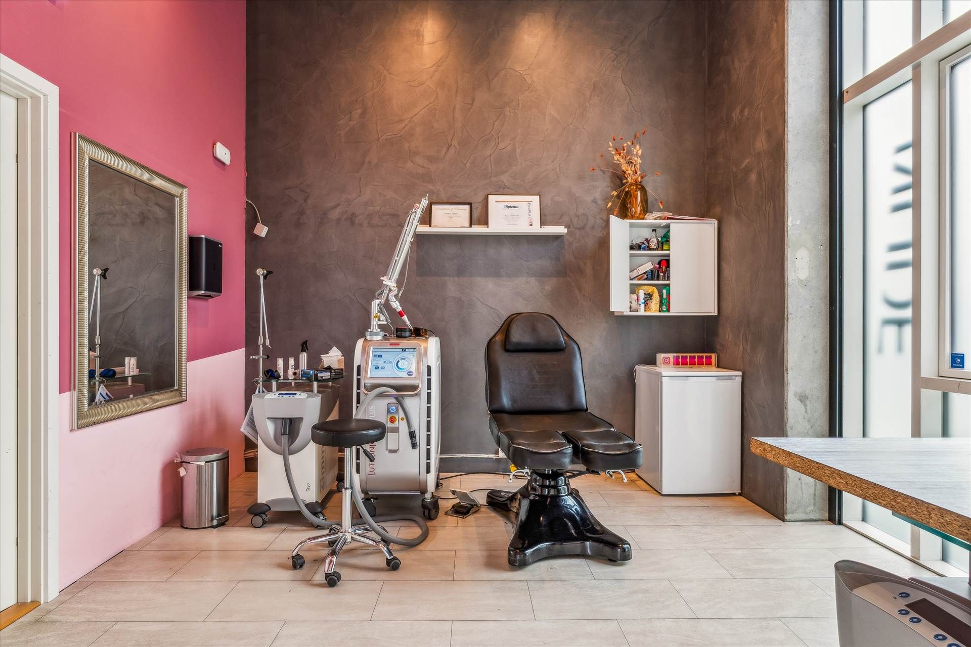 En ren og funktionel øjenvippeforlængelsessalon med moderne møbler, et lægeapparat og en hvid køleskab i en hjørne.