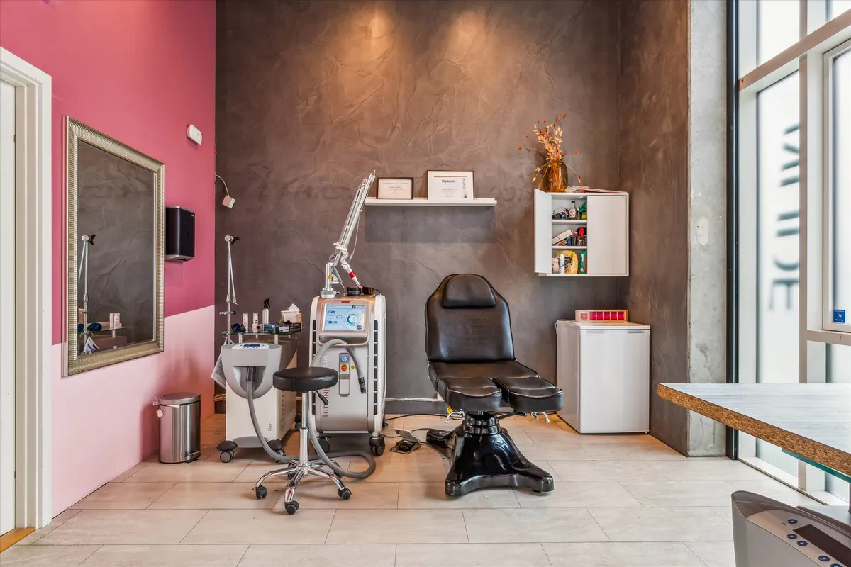 En ren og funktionel øjenvippeforlængelsessalon med moderne møbler, et lægeapparat og en hvid køleskab i en hjørne.