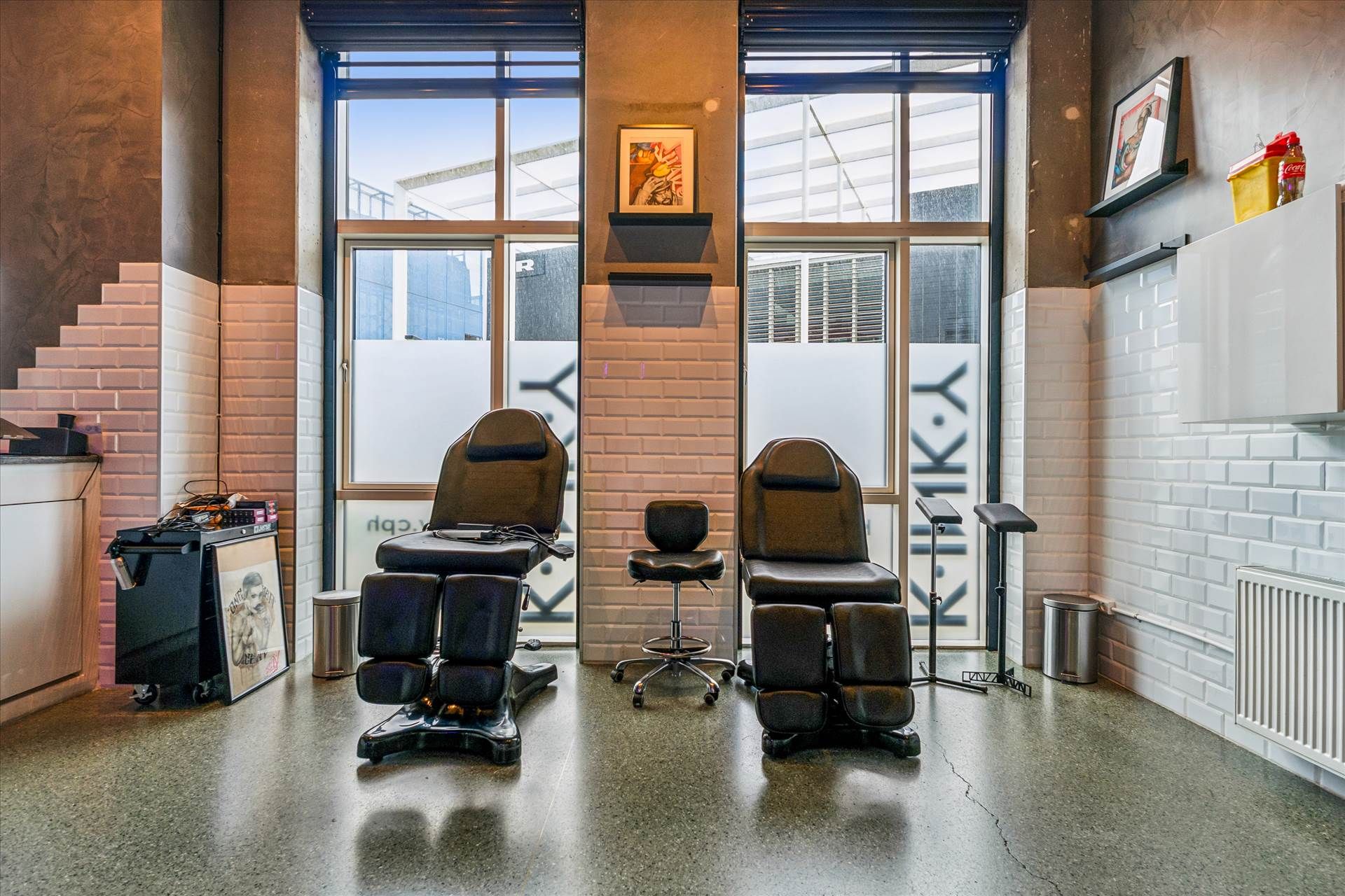 Inde i et barbersalon med højt til loftet, to læderstole og to stolpeborde med et stel i midten af rummet