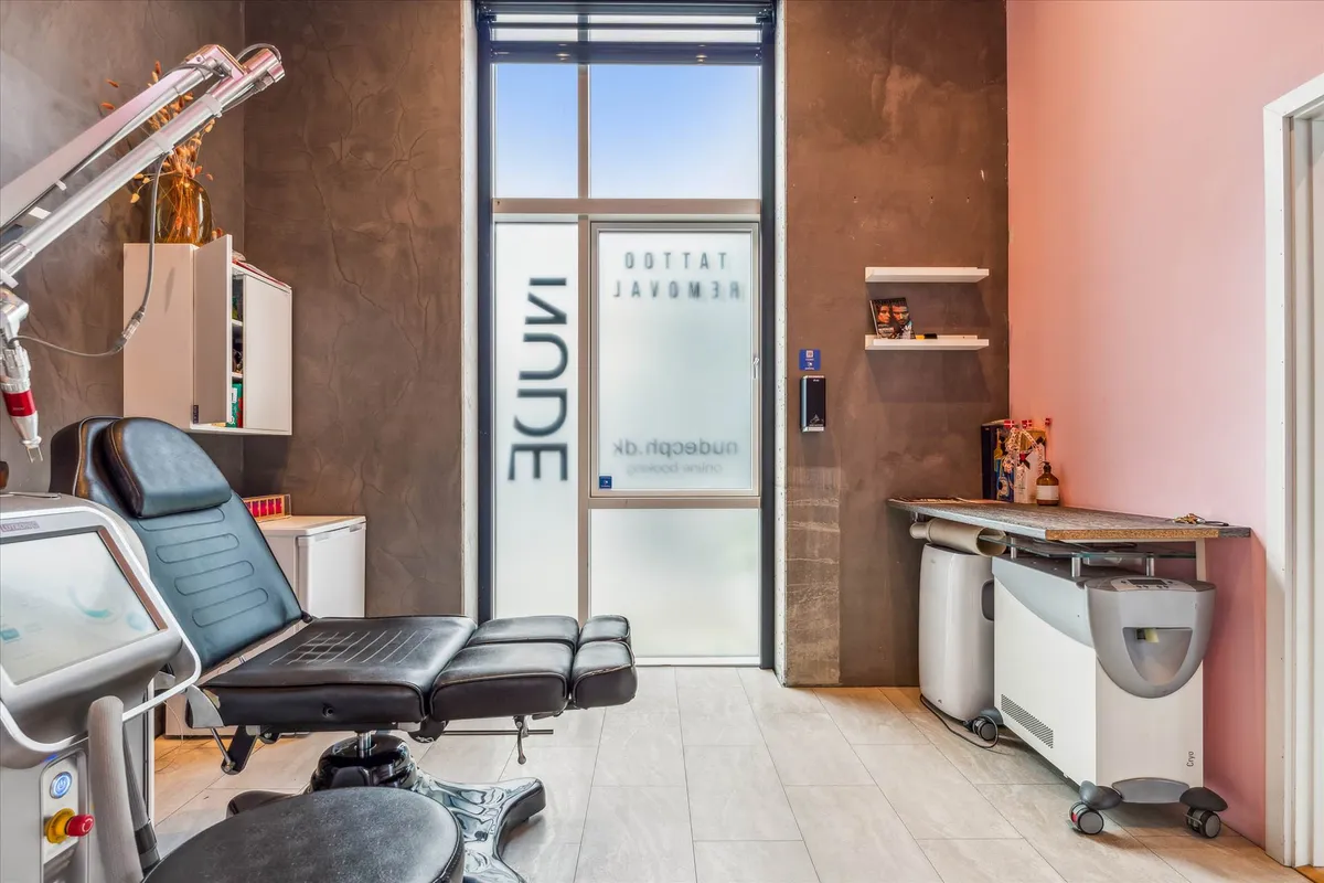 Indvendigt i et skønhedssalon med pink væg og højt loft med lyse pletter. Salonen har et stort glasdør og et stort mærke med