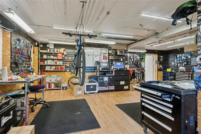 Et værksted med et stående cykelhjul og en computer skærm samt værktøj og udstyr rundt omkring i lokalet