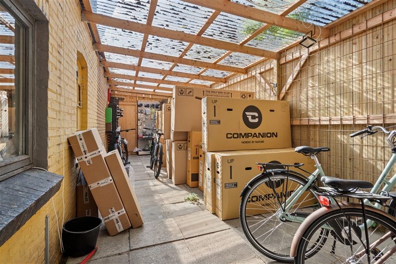 Foto af et hus med flere pakketømmer og flere cykler, hvor der er en vinduesglas og en opbevaringskasse på gulvet.