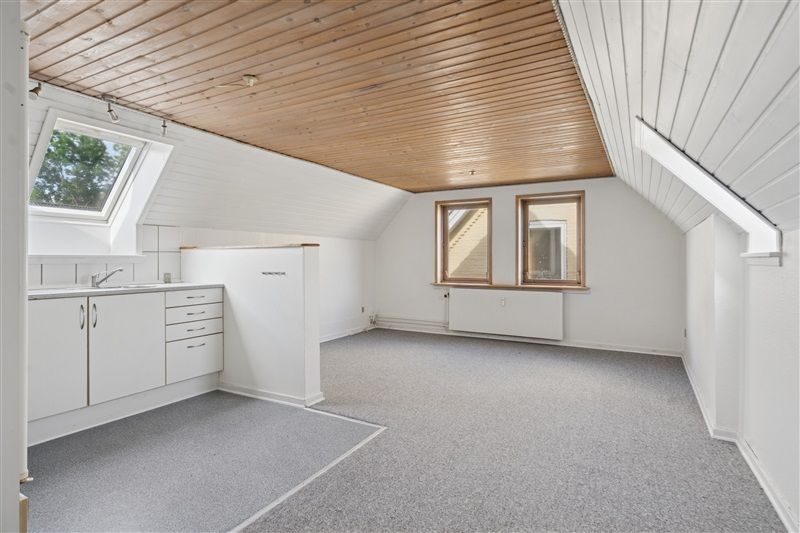 Lys og rummelig stue med højt loft og to vinduer mod syd. Hvide vægge, loft og møbler.