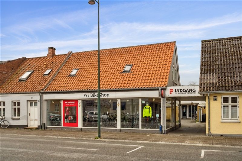 En butik med Fri Bikeshop, mange cykler og en person i gult trøje i vinduet og en gågade i baggrunden