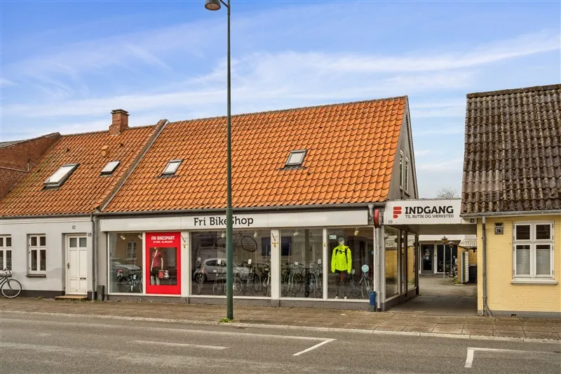 En butik med Fri Bikeshop, mange cykler og en person i gult trøje i vinduet og en gågade i baggrunden