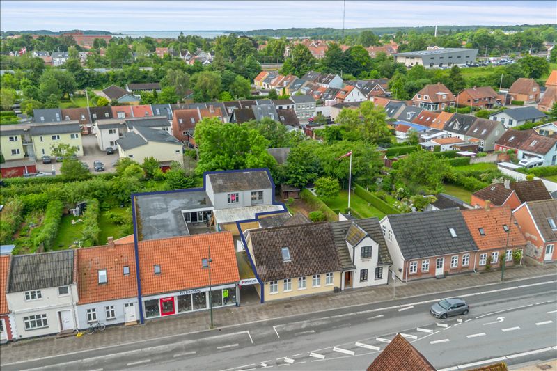 Overblik over Middelfart med ejendomme, grønne områder og en bil på vejen og et hus med et skilt foran