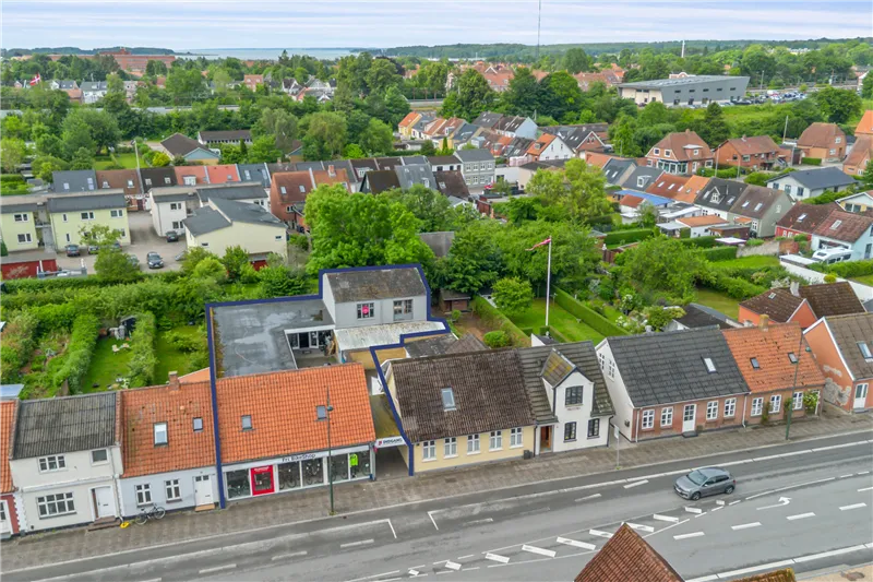Overblik over Middelfart med ejendomme, grønne områder og en bil på vejen og et hus med et skilt foran