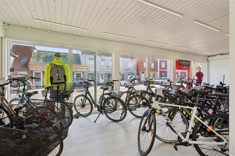En cykelforretning med mange cykler og cykelhjelme samt et skilt med teksten "Fri BikeShop"