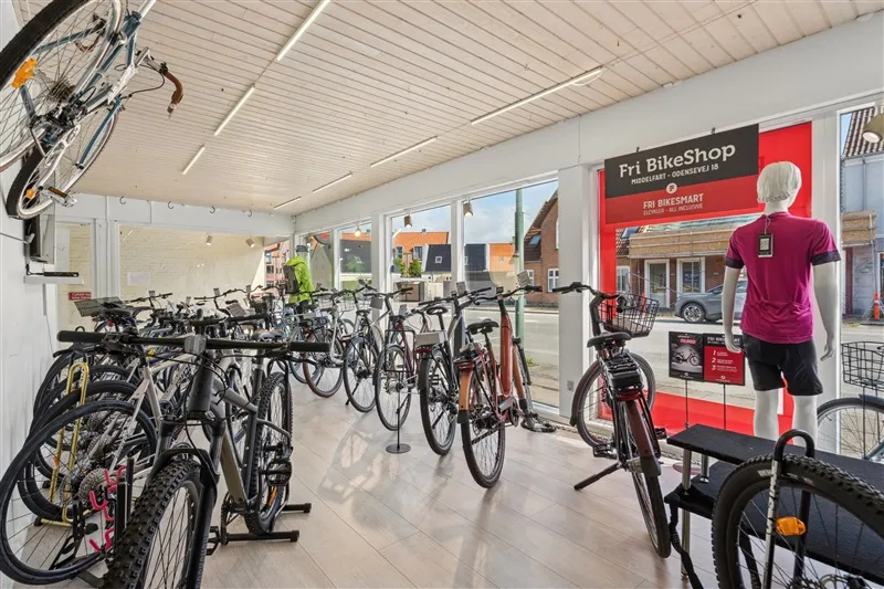 Store udvalg af cykler i butik med mærker som Fri BikeShop. Cyklerne er ophængt og stillet op på gulvet.