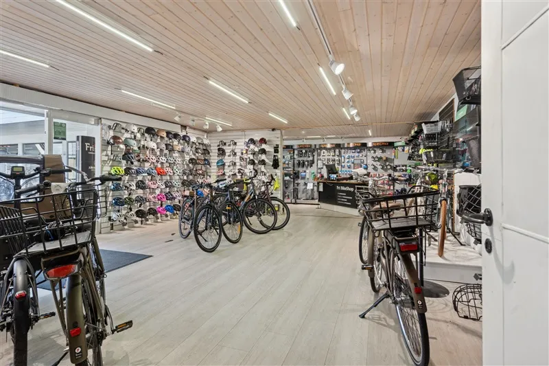 En cykelforretning med forskellige cykler og cykeludstyr. Der er hjelmhylden og salgsstande med cykeldele. Der er tre cykler