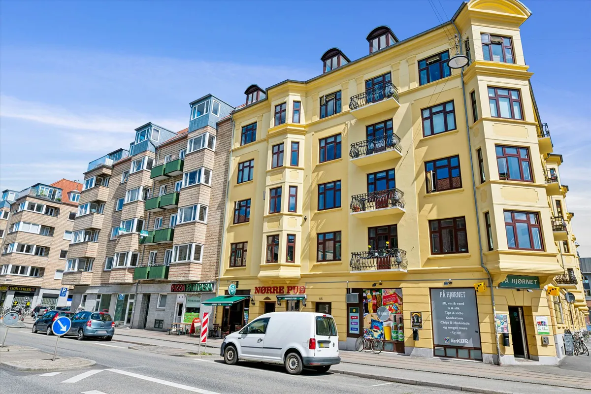 Københavnsvej med sammenbyggede bygninger, hvor det lyse gule hus har teksten Norre Pub, og en hvid varevogn er parkeret