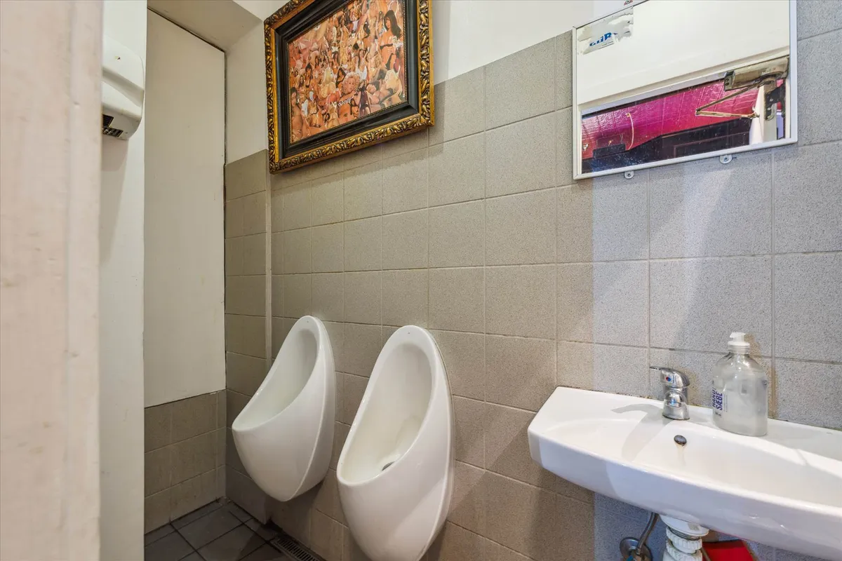 To hvide urinaler og en hvid vask i et lille badeværelse med et maleri og en spejl på væggen