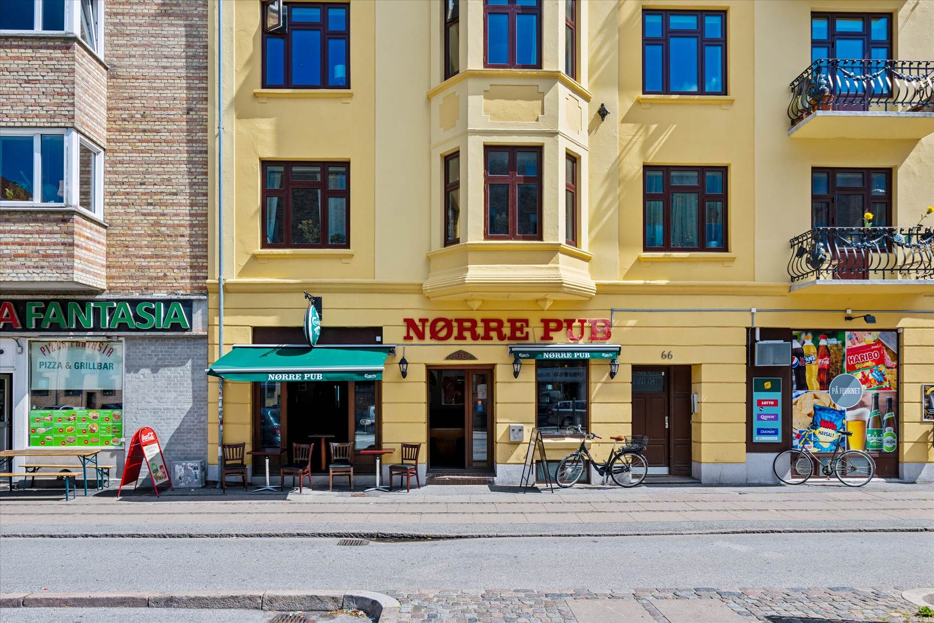 Norre Pub med grønt tage og bord og stole udenfor samt cykler foran døren og pizza restaurant til venstre