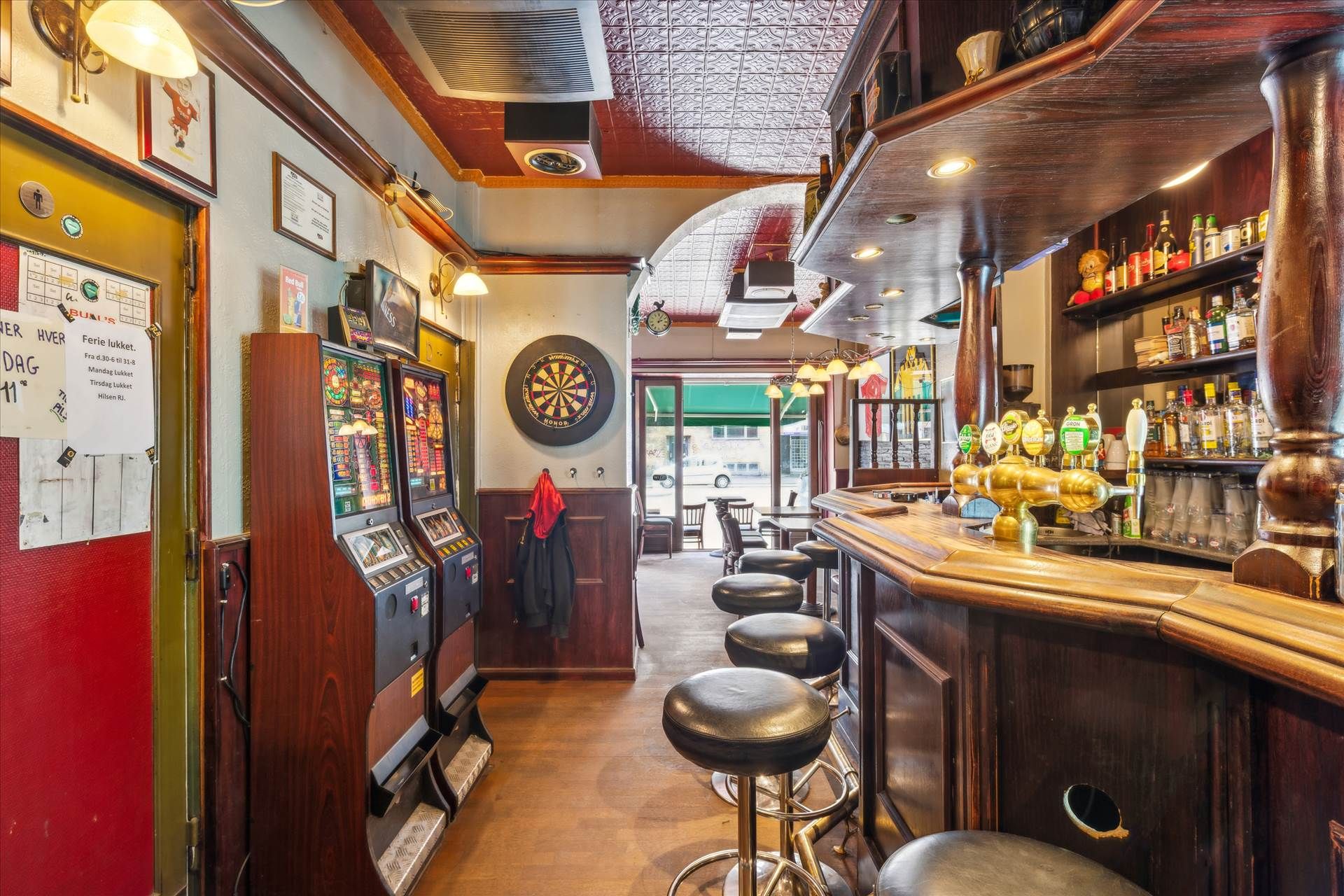 En bar med en spilleautomat, to stole og en bar, hvor der er flasker med øl og øltapper