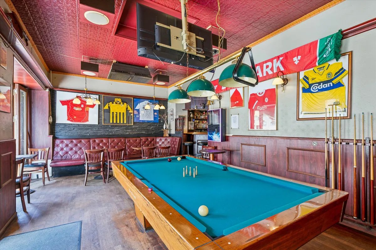 Et billardbord med et ægte hvidt bold placeret i et lokale med røde læderstole og en bar i baggrunden med en række