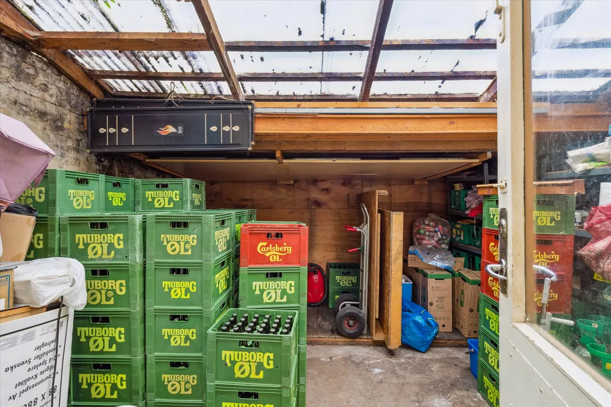 Lager med grønne ølkasser fra Tuborg ØL og røde Carlsberg ØL samt tomme kartonæsker og en rullekurv.