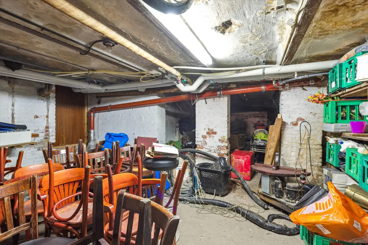 Et gammelt rum med brændstoffadtøj og røgaffald, gamle stole og træbænke samt en gammel komfur og røgaffaldspose i gulvet