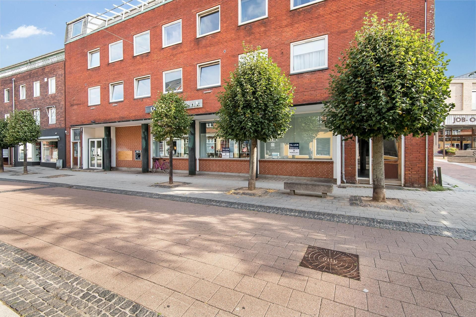 Store røde bygninger med vinduer og gulvnummer 61A og 61B. En cykel står foran den ene bygning. Der er to små træer og en