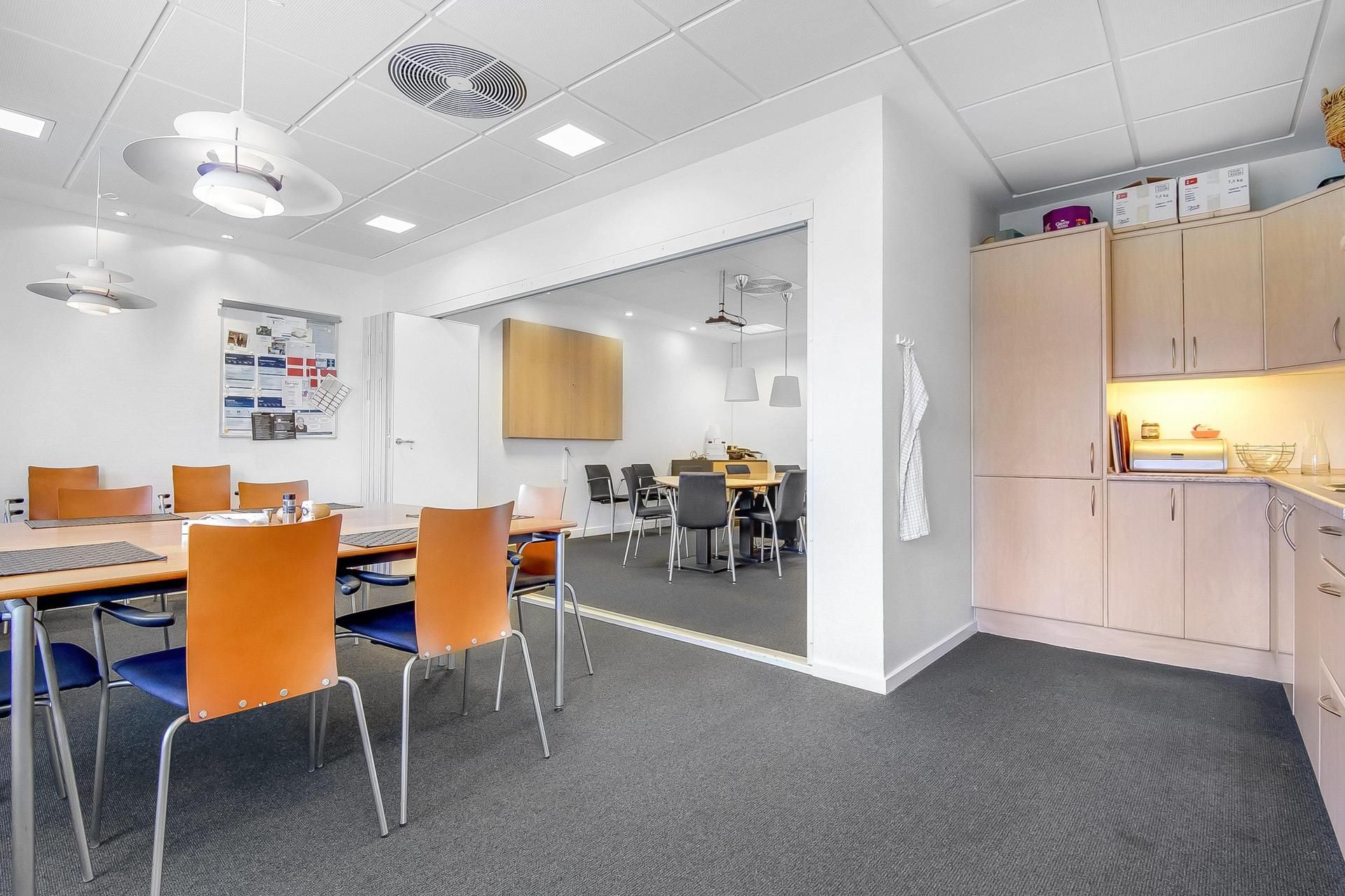 Kontorlokation med møbelsæt og stole i orange og blå. Loftventilatorer, åbne glasdøre og hængelampe. Sort og hvid skrivebræt