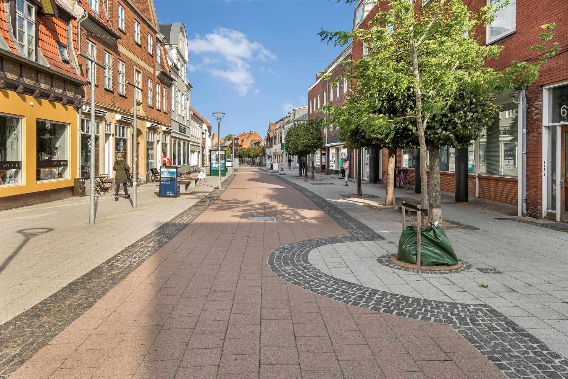 Et tomt gadebillede med røde bygninger og høje træer på hjørnerne og gulve med brolægning og gulve med granitsten