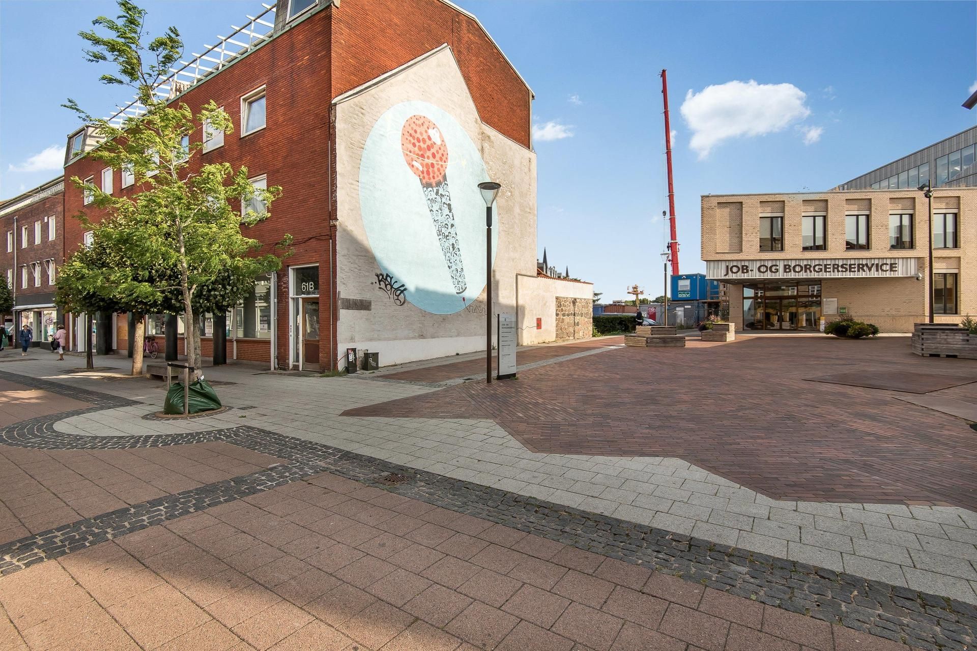 Gaden med røde mursten og et stort maleri af en mikrofon. Der er en bygning med skiltet Job og Borgerservice og en bygning